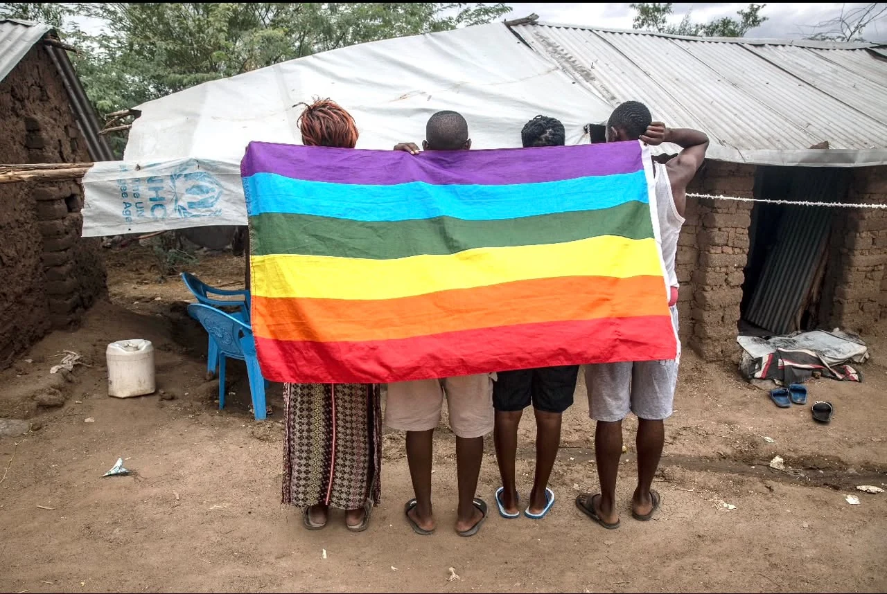 Community members standing together behind a large rainbow Pride flag
