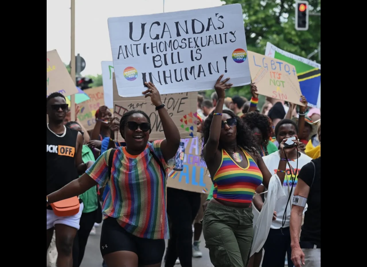 People at a public advocacy gathering holding signs calling for LGBTQ+ rights and dignity
